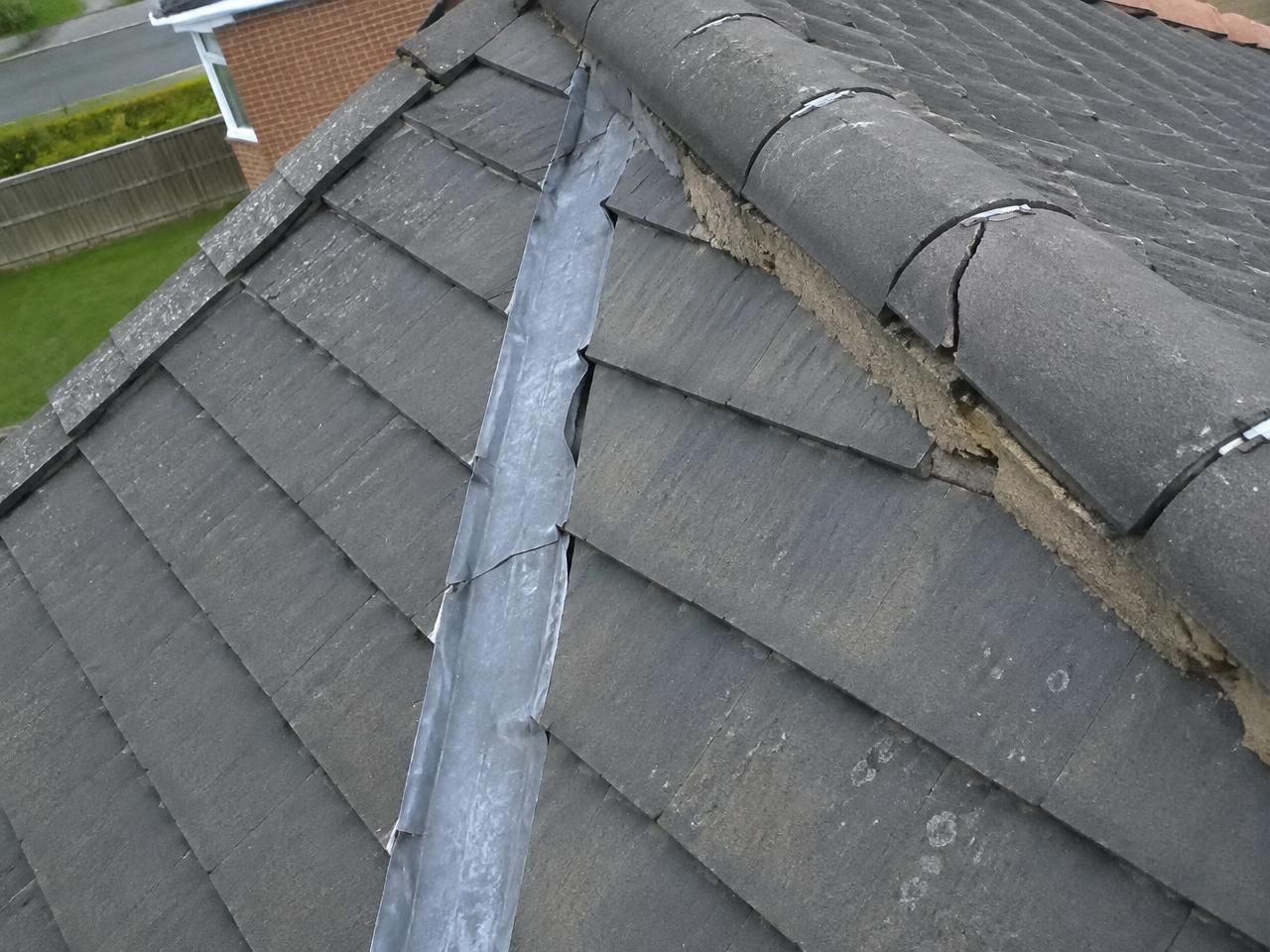 Drone aerial crop of cracked ridge tiles and poorly seated lead valley flashing